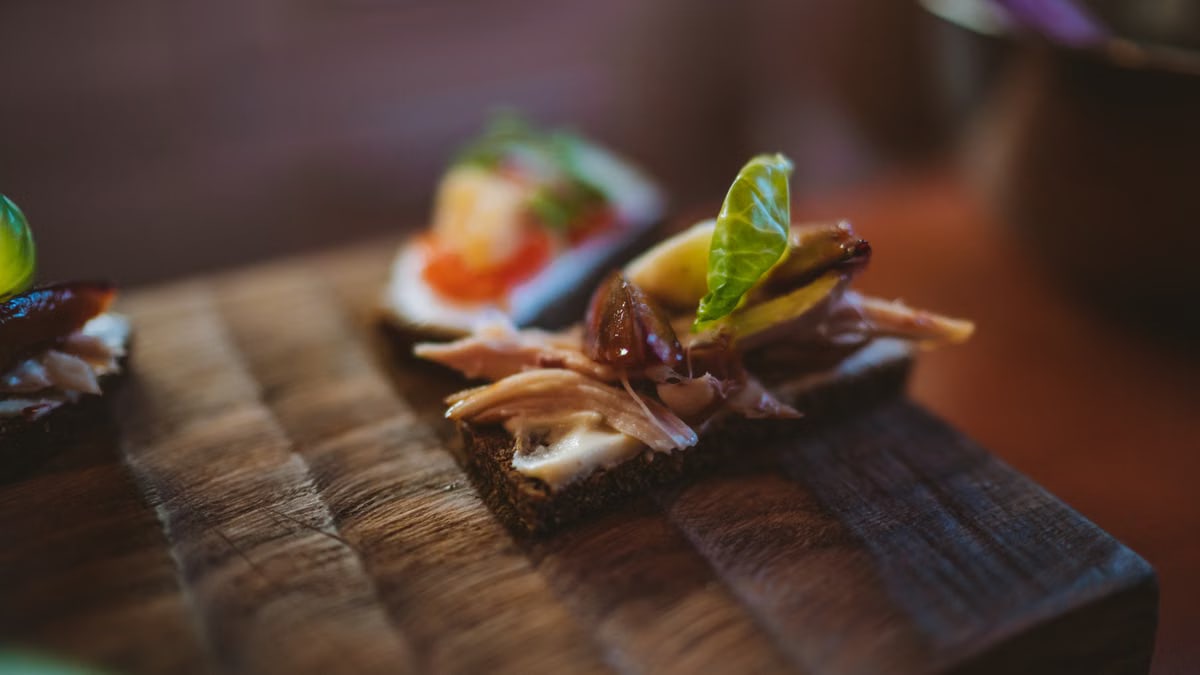 Delicious gourmet canapé with meat and greens on rustic wooden board.